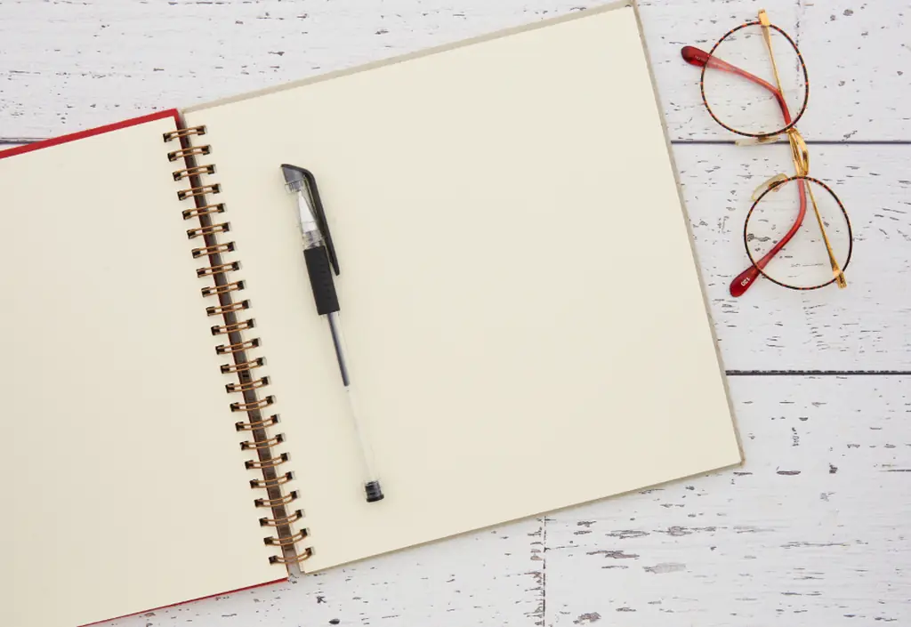 Sur une table aux teintes claires, un carnet ouvert près d’un stylo et d’une paire de lunettes