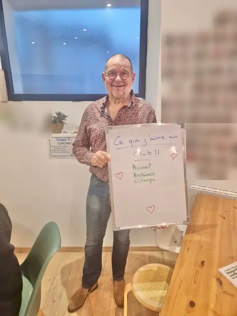 Un membre fait voir son bilan noté à l’ardoise blanche, en pleine salle